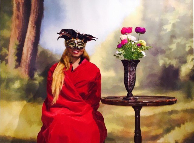 Africah dressed in a red velvet cloak and masquerade mask for a 19th Century Photoshoot.